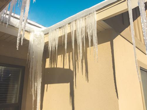 Icicles hang down near a valley of a roof, and ice is built up 2-3 inches high on the shingles. 